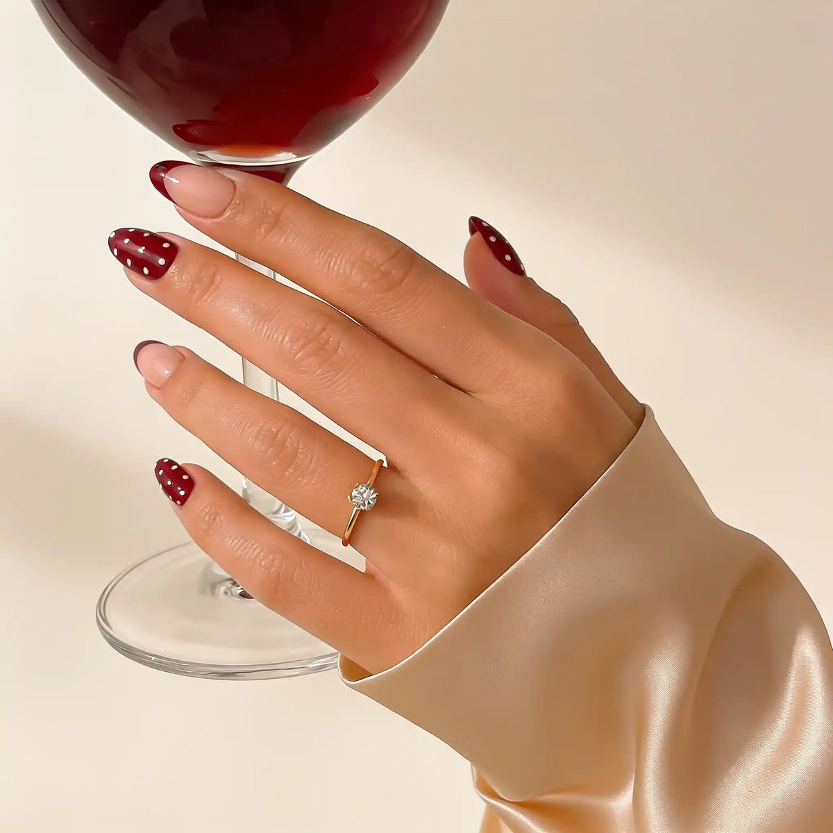„Cherry Kiss“ – kurze, mandelförmige, kirschrote, gemusterte Nägel an der Hand neben einem Weinglas von Aimee STHLM