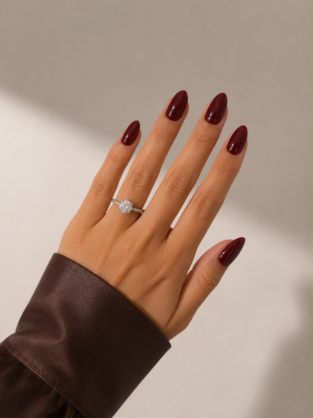 Eine Hand im wunderschönen Licht, an der die kurzen, mandelförmigen (Short Almond) weinroten Press-on-Nägel „French Wine“ von Aimee STHLM getragen werden